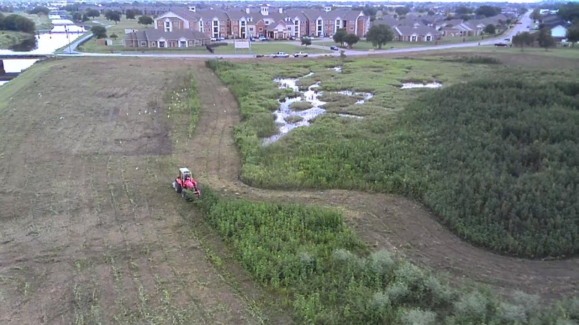 Aerial view of a tractor brush hogging an overgrown field in Port Arthur, TX